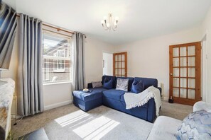 A living room with a sectional sofa, a chandelier, and a view through a window with curtains. - Stylish 3BR, Warwick Hosp, Contractor long stays (Warwick)