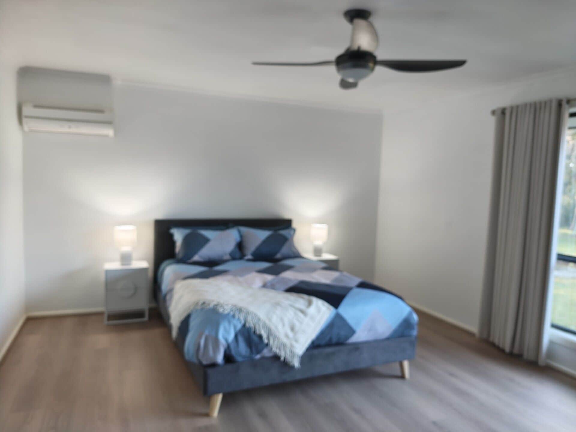 Een slaapkamer met een bed, een plafondventilator, bedlampen en een raam met gordijnen.