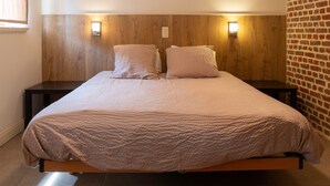 Una cama con cabecera de madera, dos mesitas de noche y una pared de ladrillo.