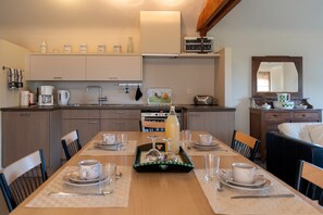 A modern kitchen with a dining table set for two, equipped with a coffee maker, kettle, and a radio. - Apartment 3 - Enjoy a Cozy Stay at the Alfonsinehoeve (Heers)
