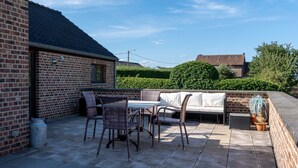 Un patio con pared de ladrillo, una mesa con sillas y una zona de estar con cojines.