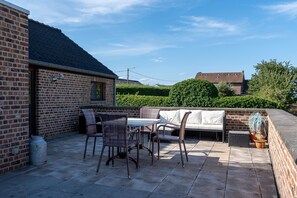 A patio area with a brick wall, a table with chairs, and a cushioned seating area. - Apartment 3 - Enjoy a Cozy Stay at the Alfonsinehoeve (Heers)