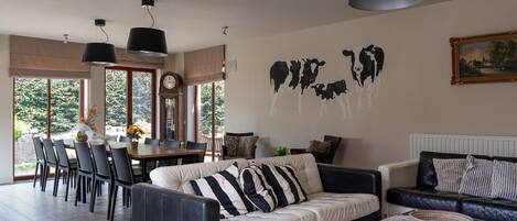 Ein Wohnzimmer mit einer Couch, einem Esstisch und Stühlen. An der Wand hängt eine Uhr und ein Gemälde von Kühen.
