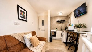 Um espaço de estar compacto com um sofá marrom, uma cozinha e uma TV de tela plana na parede.
