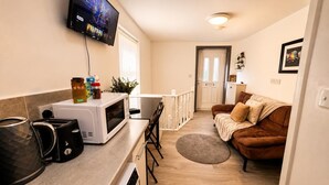 Um espaço compacto com cozinha americana, televisão na parede, sofá marrom e uma porta que dá para outro quarto.