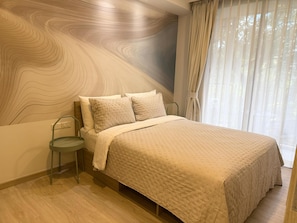 A bedroom with a bed, a nightstand, a wall with a wood grain pattern, and a window with curtains. - Skypark Laguna 1BR, Rooftop Pool, Walk to Bang Tao & Boat Avenue (Sakhu)