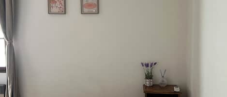 Een slaapkamer met een bed, kussens, een nachtkastje met een vaas en kaarsen, en twee foto’s in lijsten aan de muur.