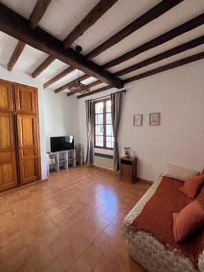 A room with a bed, a TV, a wooden wardrobe, and a window with curtains. - Typical Arles-style house from the 1970s - air conditioning - sleeps 4 - downtown (Arles)