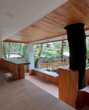 A wooden interior with a bar area, a large black column, and a view of the outdoors. - Cozzy Muara Rahong Hills (Pangalengan)