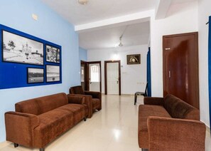 A room with two brown sofas, a white door, and a blue wall with framed pictures. - Classic Cochin Apartments Annex (Aluva)