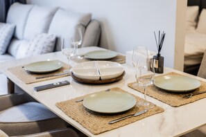 A dining table set with plates, cutlery, and glasses, with a remote control and a candle on the table. - Skypark Laguna 2BR, Golf View, Rooftop Pool (Cherngtalay)