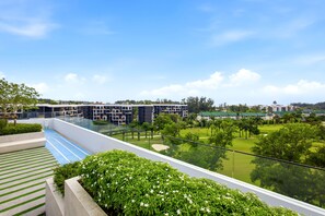 A modern building with a glass balcony overlooking a well-maintained lawn and a golf course. - Skypark Laguna 2BR, Golf View, Rooftop Pool (Cherngtalay)