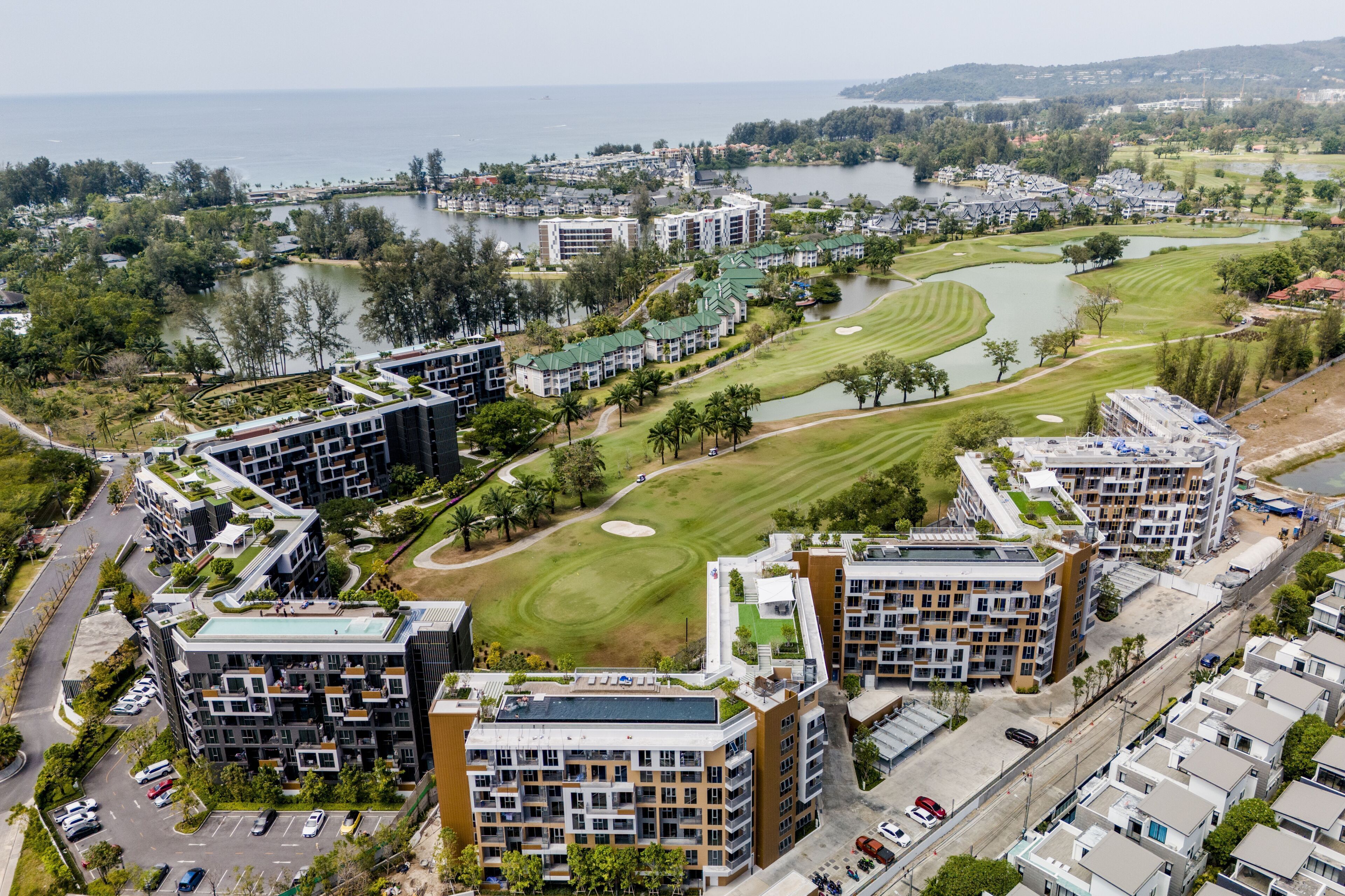 A modern residential area with apartment buildings, a golf course, and a body of water.