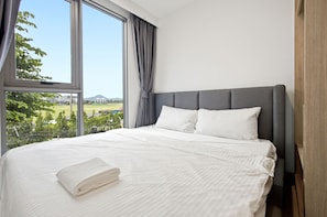 Et hotelværelse med et stort vindue, en seng med hvide sengetøj og en grå sengegavl.