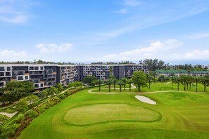 A modern multi-story building with a landscaped golf course in the foreground. - Skypark Laguna 2BR, Golf View, Rooftop Pool (Cherngtalay)