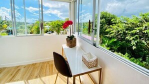 Une pièce avec une grande fenêtre, un plancher en bois, une table blanche, une chaise noire et une plante en pot.