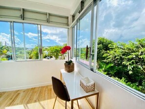 A room with a large window, a wooden floor, a white table, a black chair, and a potted plant. - Les Orchidées de Sainte-Anne Vacation Rentals: Pool and Hot Tub (Sainte-Anne)