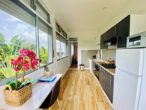 A modern kitchen with a view of the outdoors, a dining area with a bench, and a kitchen counter with appliances. - Les Orchidées de Sainte-Anne Vacation Rentals: Pool and Hot Tub (Sainte-Anne)