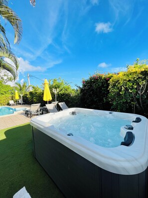 A hot tub surrounded by a pool, lounge chairs, and yellow umbrellas. - Les Orchidées de Sainte-Anne Vacation Rentals: Pool and Hot Tub (Sainte-Anne)