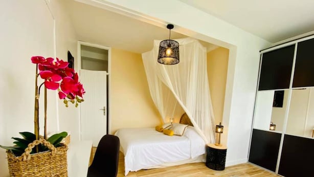 Une chambre à coucher avec un lit, une table de chevet avec une lampe, une chaise, un panier en osier et une grande fenêtre.