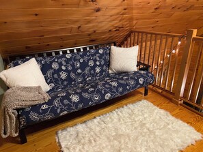 A wooden cabin interior with a sofa, two pillows, a fluffy rug, and a wooden staircase. - Cozy 3-bedroom cabin in delightful Monroe with AC and treadmill (Monroe)