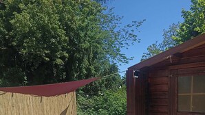 Eine Außenpatio-Terrasse mit rundem Tisch und Stühlen, einer überdachten Sitzgelegenheit und einem Holzbau im Hintergrund.