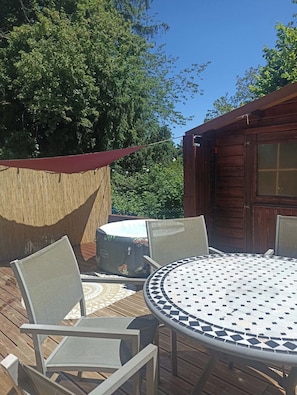 Eine Außenpatio-Terrasse mit rundem Tisch und Stühlen, einer überdachten Sitzgelegenheit und einem Holzbau im Hintergrund.