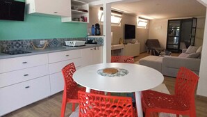 Eine moderne Küche mit weißen Schränken, einem Esstisch mit roten Stühlen und einer Wohnbereich mit einer Couch und einem Fernseher.