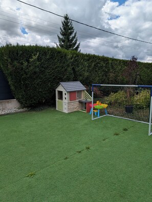 Ein Garten mit Kunstgrashalm, einem kleinen Spielhäuschen und einem Fußballtor.