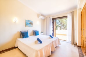 A hotel room with two beds, a painting on the wall, an air conditioning unit, and a view of the outdoors through a glass door. - Charming Villa with Heatable Pool and BBQ (Albufeira)
