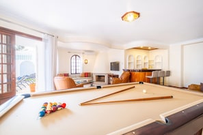 A pool table with balls and cues, a sofa, a television, and a bar area with stools. - Charming Villa with Heatable Pool and BBQ (Albufeira)