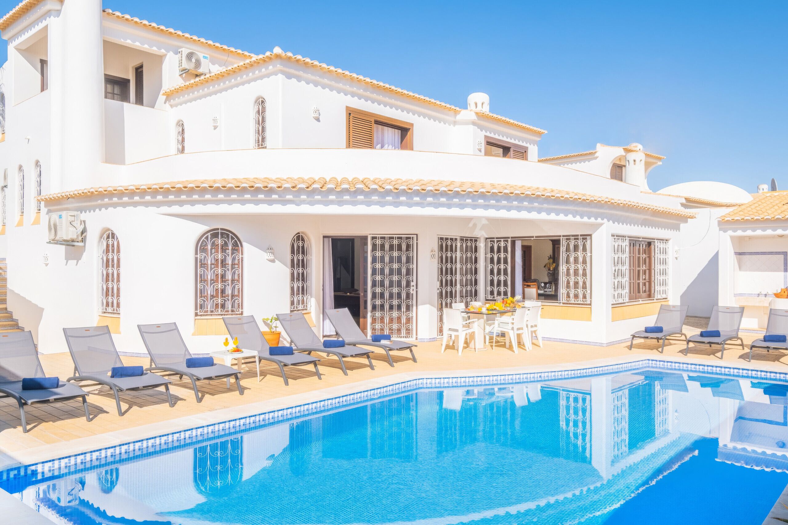 A white villa with a pool, sun loungers, and a dining area.