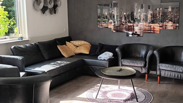 Ein modernes Wohnzimmer mit einem Ecksofa, zwei Sesseln, einem Couchtisch und einem Stadtbild an der Wand.