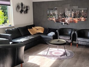 A modern living room with a sectional sofa, two armchairs, a coffee table, and a cityscape artwork on the wall. - 5 Star Holiday Home in Olsted (Olsted)