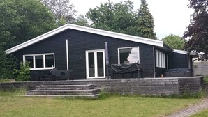 Ein zweistöckiges Haus mit überdachter Terrasse und einer Sitzgruppe im Freien.