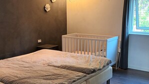 Ein Schlafzimmer mit einem Bett, einem weißen Babybett, einem Nachttisch und einem Fenster mit Vorhängen.
