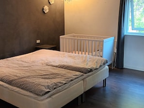 A bedroom with a bed, a white crib, a nightstand, and a window with curtains. - 5 Star Holiday Home in Olsted (Olsted)