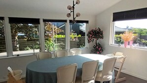 Ein Essbereich mit einem runden Tisch, sechs Stühlen und Blick ins Freie durch große Fenster.