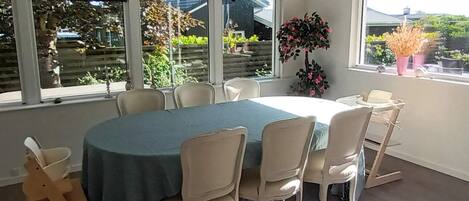 A dining area with a round table, six chairs, and a view of the outdoors through large windows.