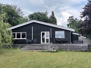 A black building with a flat roof, large windows, and a covered outdoor seating area. - 5 Star Holiday Home in Olsted (Olsted)