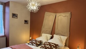 A bedroom with a bed, two bedside lamps, a decorative ceiling light, and a window with curtains.