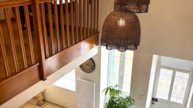 A staircase with wooden railings, a clock on the wall, a potted plant, and a white door with decorative ironwork.