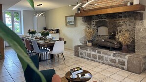 A dining area with a brick fireplace, a dining table set for four, and a kitchen in the background.