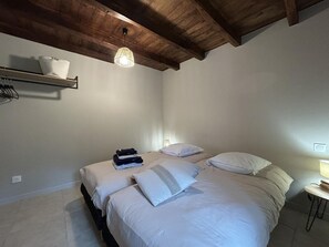 Une chambre avec deux lits, un plafond en bois, une étagère avec un panier et une petite table avec une lampe.