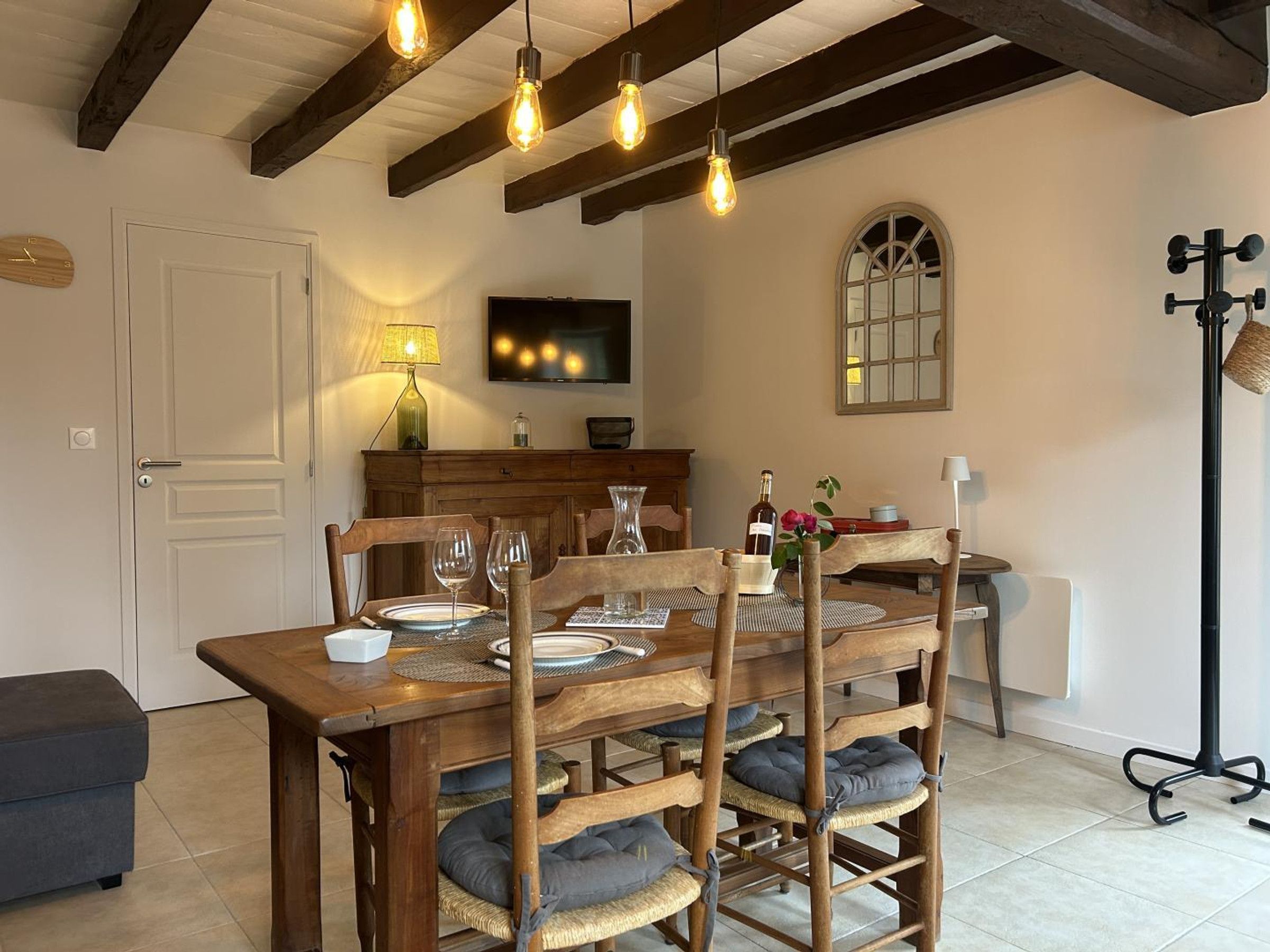 A dining area with a wooden table set for four, a television above it, and a lamp on the wall.