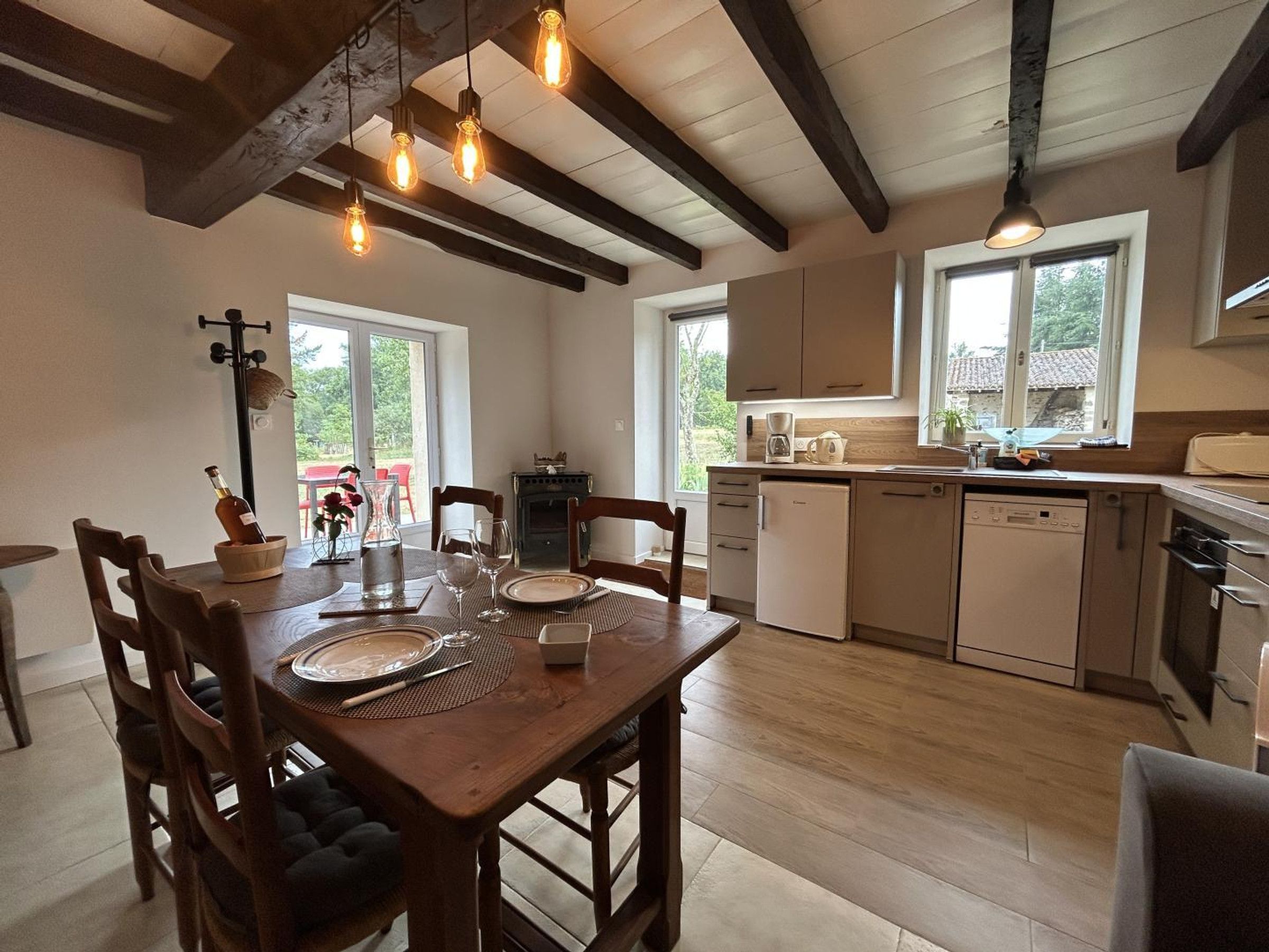 A dining area with a wooden table set for four, a coffee machine, and a view of the outdoors through a window.