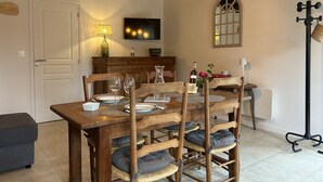 A dining area with a wooden table set for four, a television above it, and a lamp on the wall. - Independent house in nature - 4 guests (Esse)