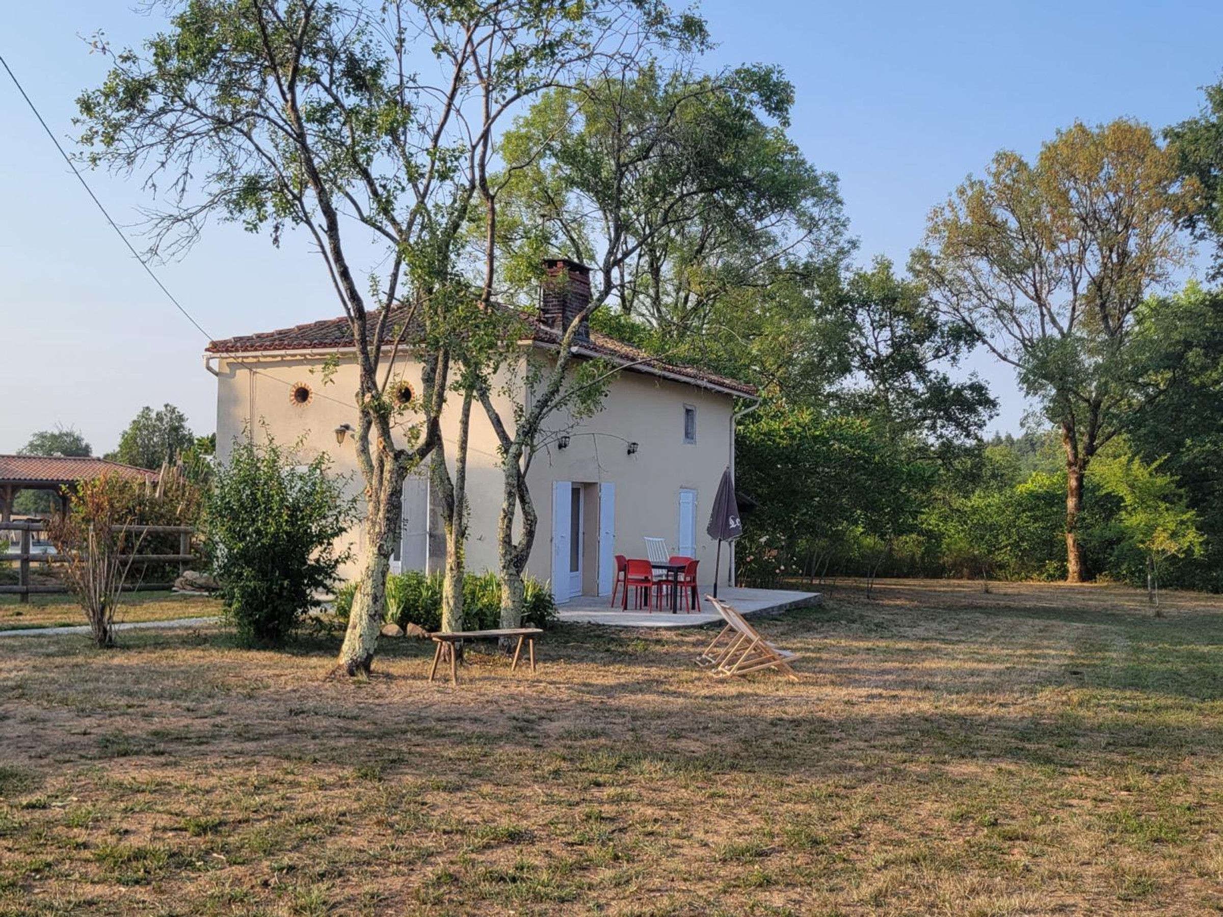 A single-story building with a flat roof, a small porch with a table and chairs, and a fenced yard.