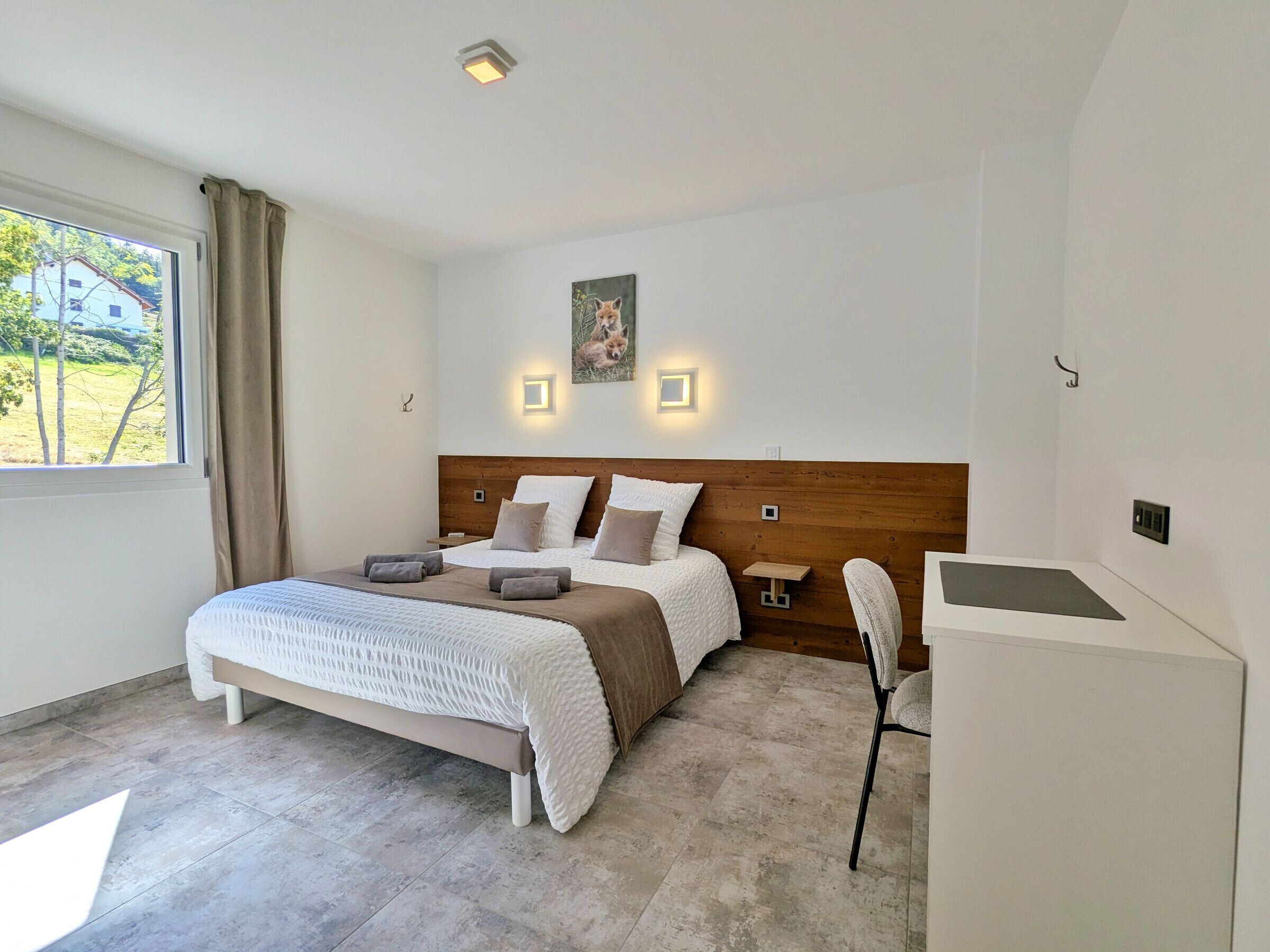A bedroom with a bed, bedside tables, a desk, and a window with curtains.