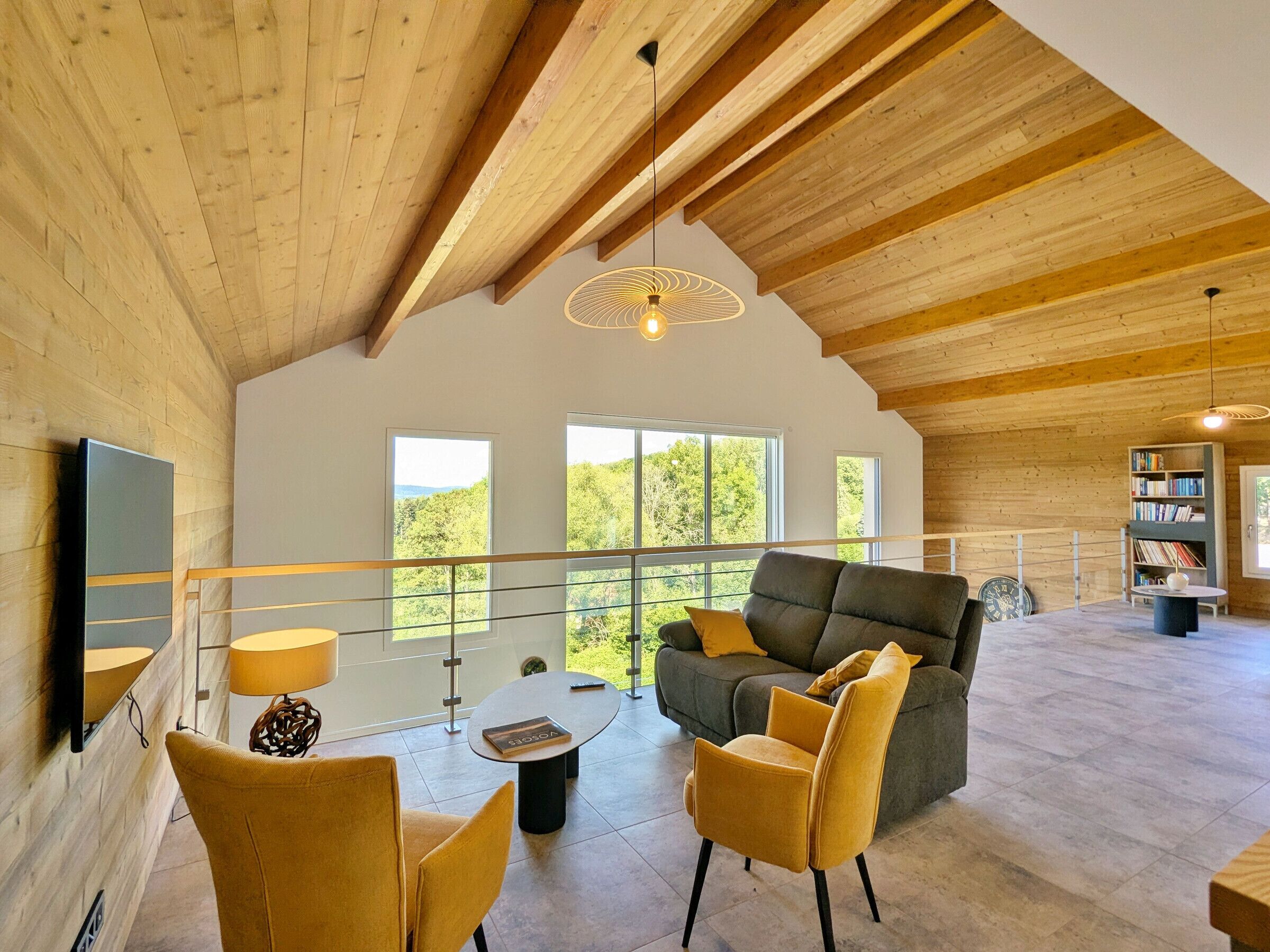 A spacious living area with a high ceiling, wooden beams, a sofa, chairs, a coffee table, and a bookshelf.
